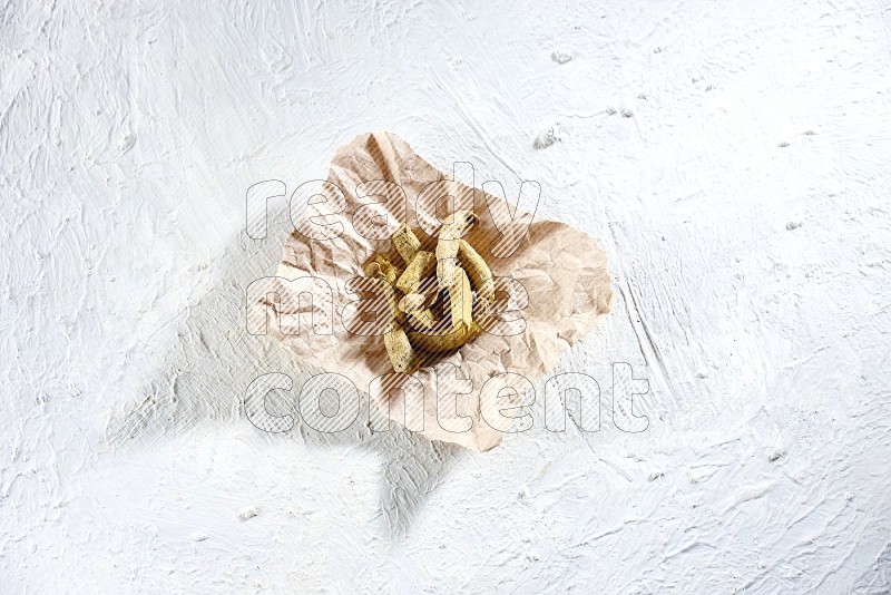 Dried turmeric whole fingers in a crumpled piece of paper on textured white flooring