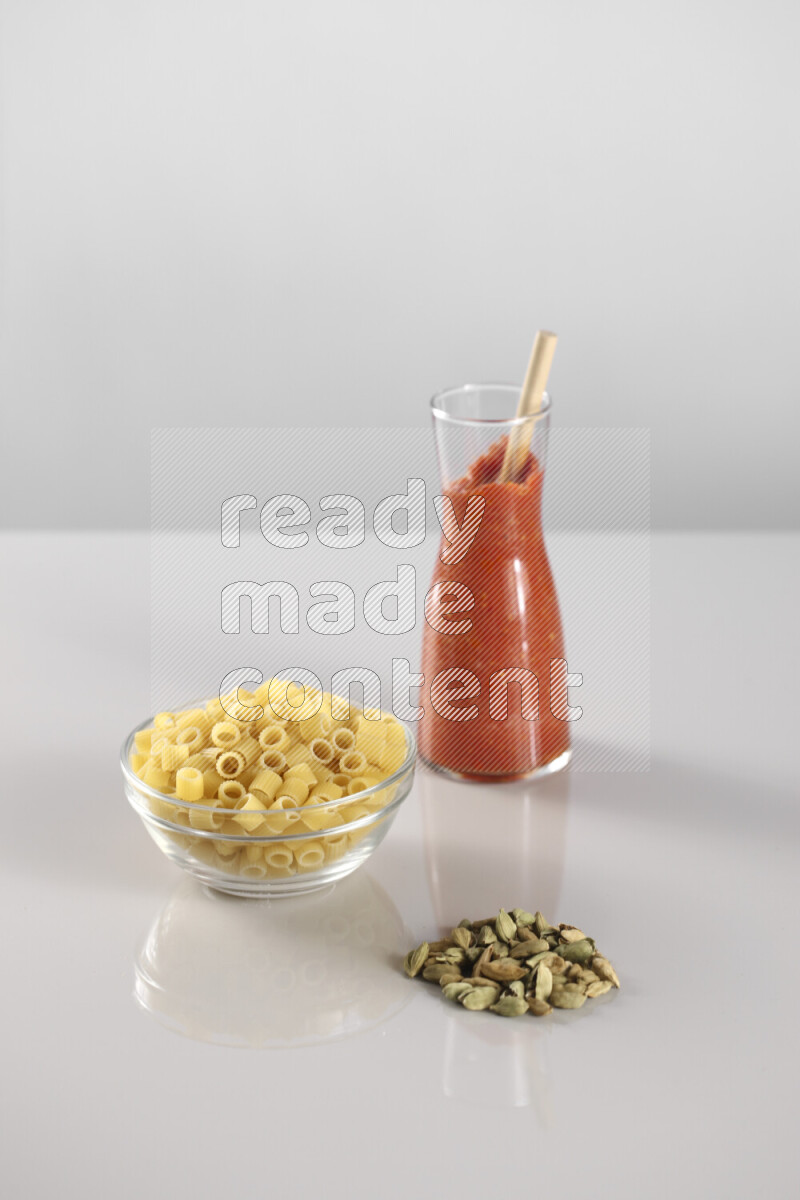 Raw pasta with tomatoe pasta with different ingredients such as cherry tomatoes, basil, garlic, bay laurel, cardamom, white pepper, black pepper, red chilis and wheat stalks on light grey background