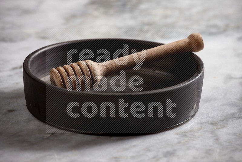 Black Pottery Oven Plate with wooden honey handle in it, on grey marble flooring, 15 degree angle
