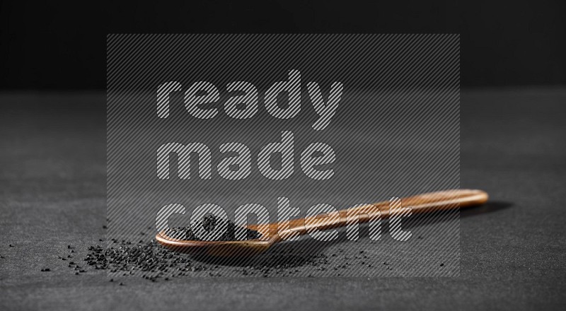 A wooden ladle full of black seeds and the seeds spread beside it on a black flooring