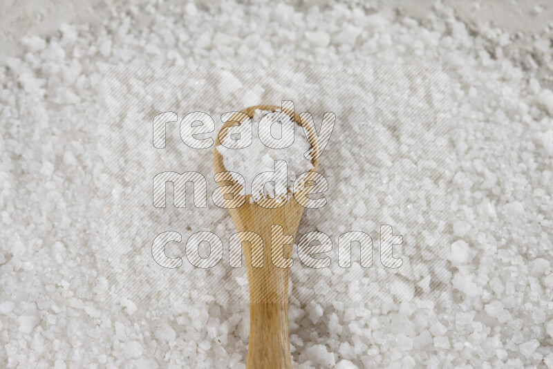 A wooden spoon full of white salt on white background