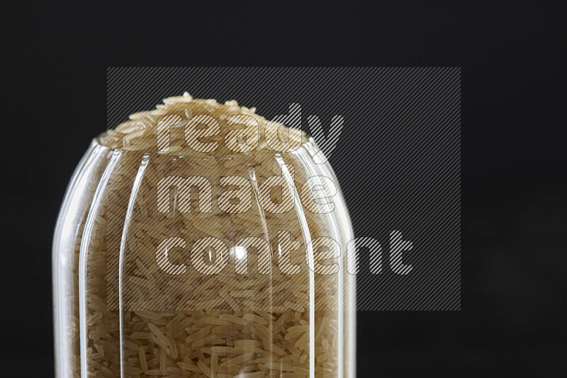 Basmati golden rice in a glass jar on black background