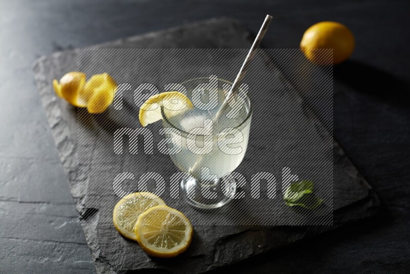 A glass of lemon juice with a straw on black background