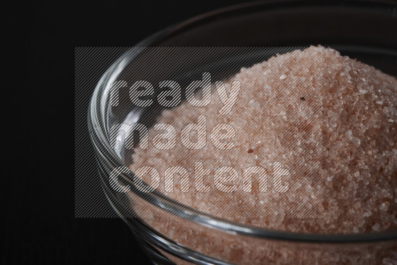 A glass bowl full of fine himalayan salt on black background