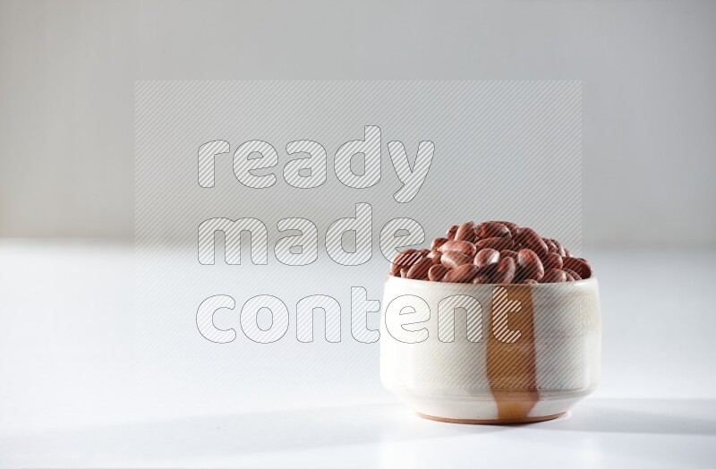 A beige ceramic bowl full of red skin peanuts on a white background in different angles