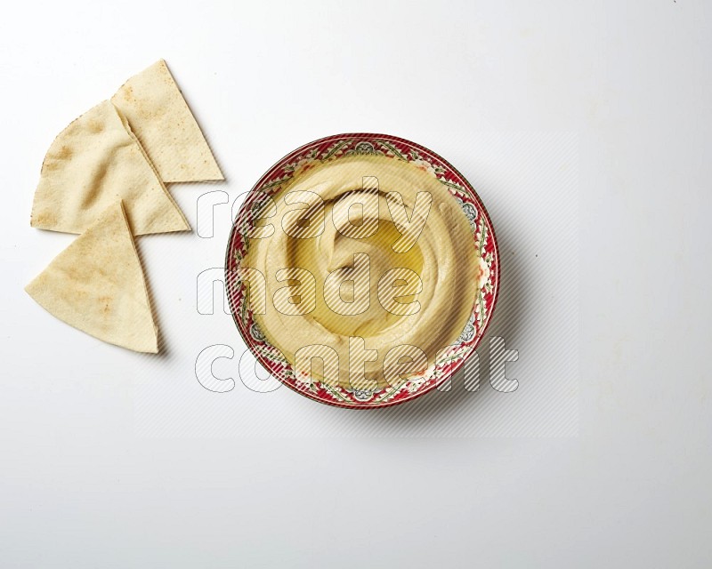 Hummus in a red plate with patterns garnished with olive oil on a white background