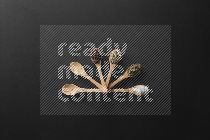 الفلفل الأبيض والقرنفل والهيل والملح والفلفل الأسود وريحان مجفف في معالق خشبية علي خلفية سوداء