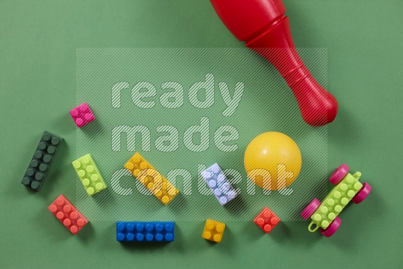 Plastic building blocks, balls and bowling pins on green background in top view (kids toys)