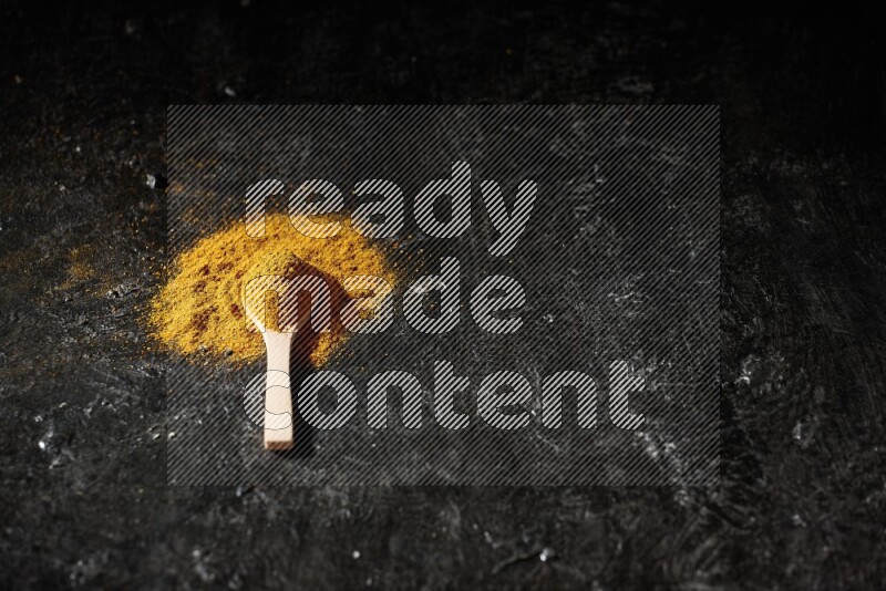 A wooden spoon full of turmeric powder on textured black background