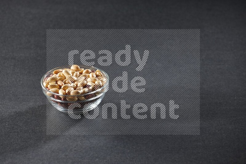 A glass bowl full of peeled peanuts on a black background in different angles