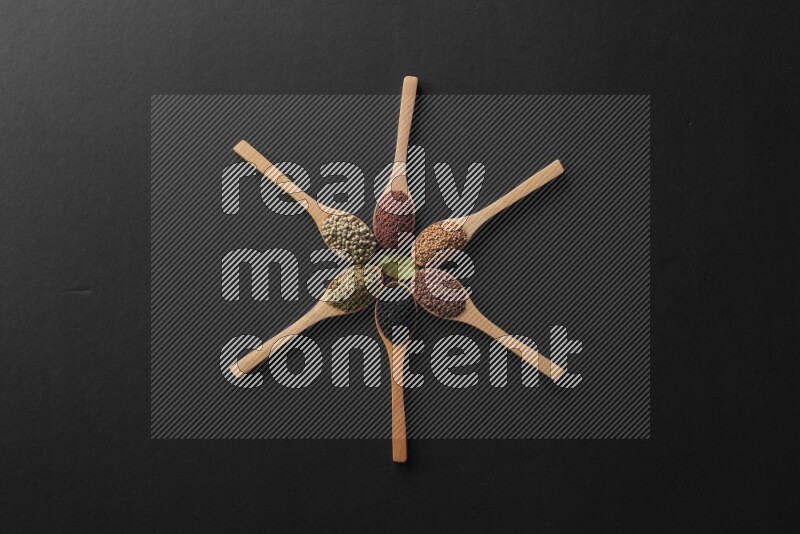 wooden spoons filled with white peppers, mustard seeds, black seeds, garden cress, cumin and flax on black flooring and shaped like a clock