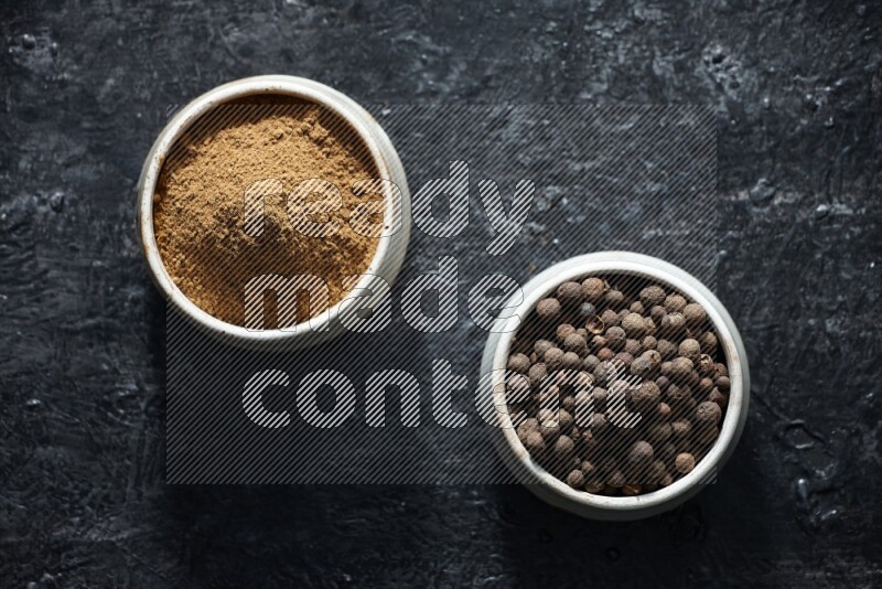 2 beige bowls, one full of allspice powder and the other full of whole balls on a textured black flooring
