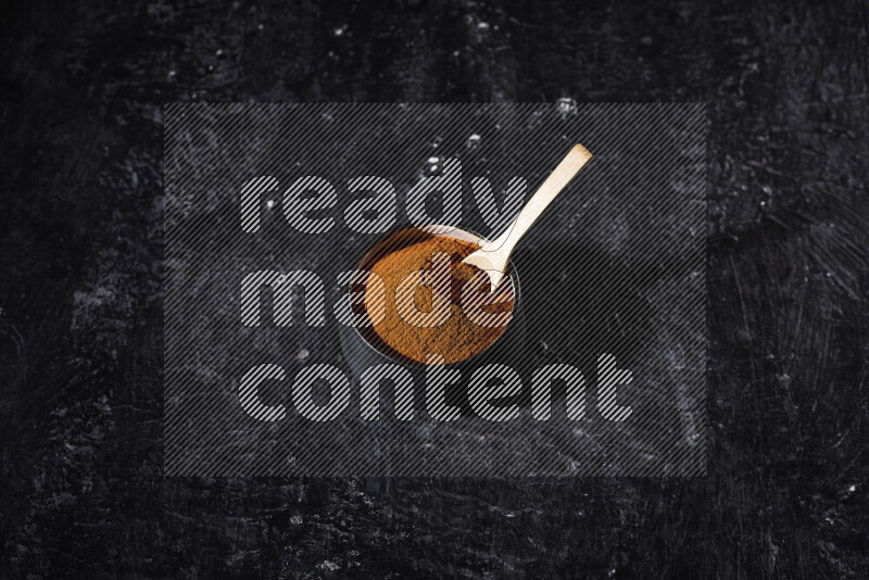 A black pottery bowl full of ground paprika powder on black background