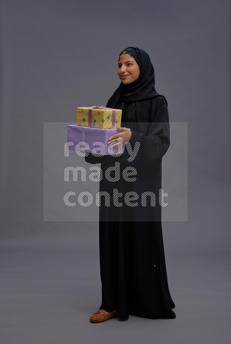 Saudi woman wearing Abaya standing holding gift box on gray background
