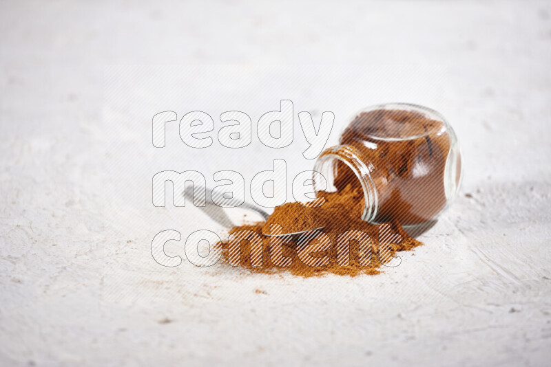 A glass jar full of ground paprika powder flipped with some spilling powder on white background