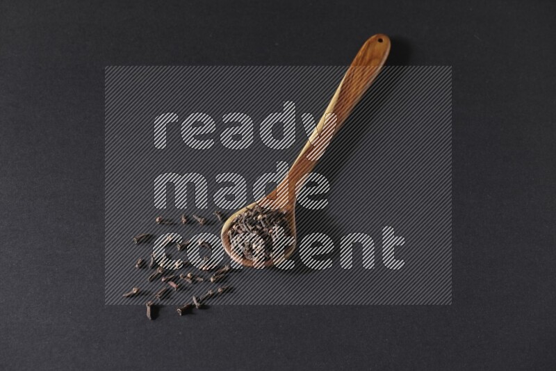 حبوب القرنفل في ملعقة خشبية علي خلفية سوداء