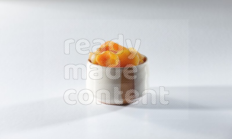A beige ceramic bowl full of dried apricots on a white background in different angles