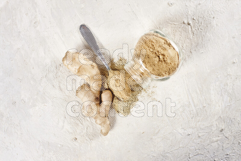 A glass jar full of ground ginger powder flipped with some spilling powder on white background