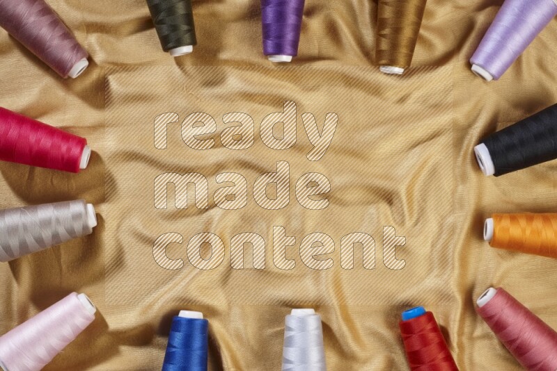 Multicolored sewing thread spools on yellow fabric background