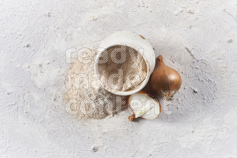 A beige pottery bowl full of onion powder with fallen powder from it on white background