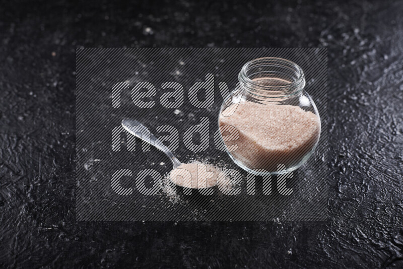 A glass jar full of fine himalayan salt on black background