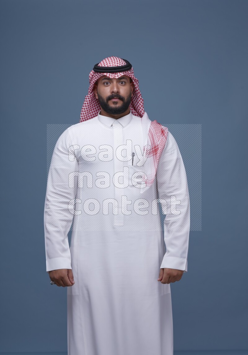 A man pointing on blue background wearing Saudi Thob with Shomag