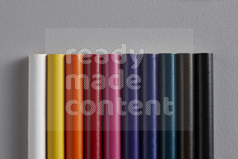 A collection of colored pencils arranged showcasing a gradient of different hues on grey background