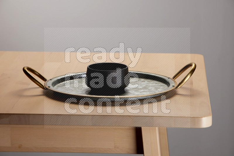 black bowl placed on a rounded stainless steel tray with golden handels on the edge of wooden table