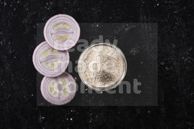 A glass jar full of onion powder on black background