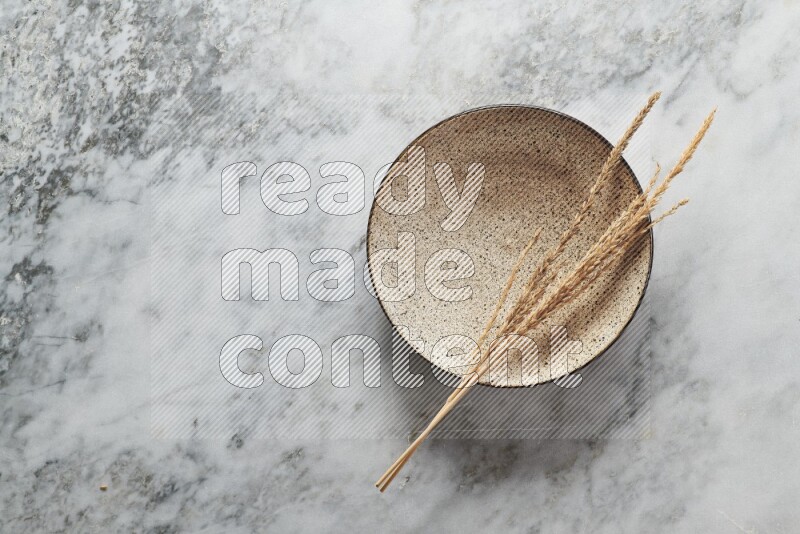 Wheat stalks on multicolored pottery plate on grey marble background