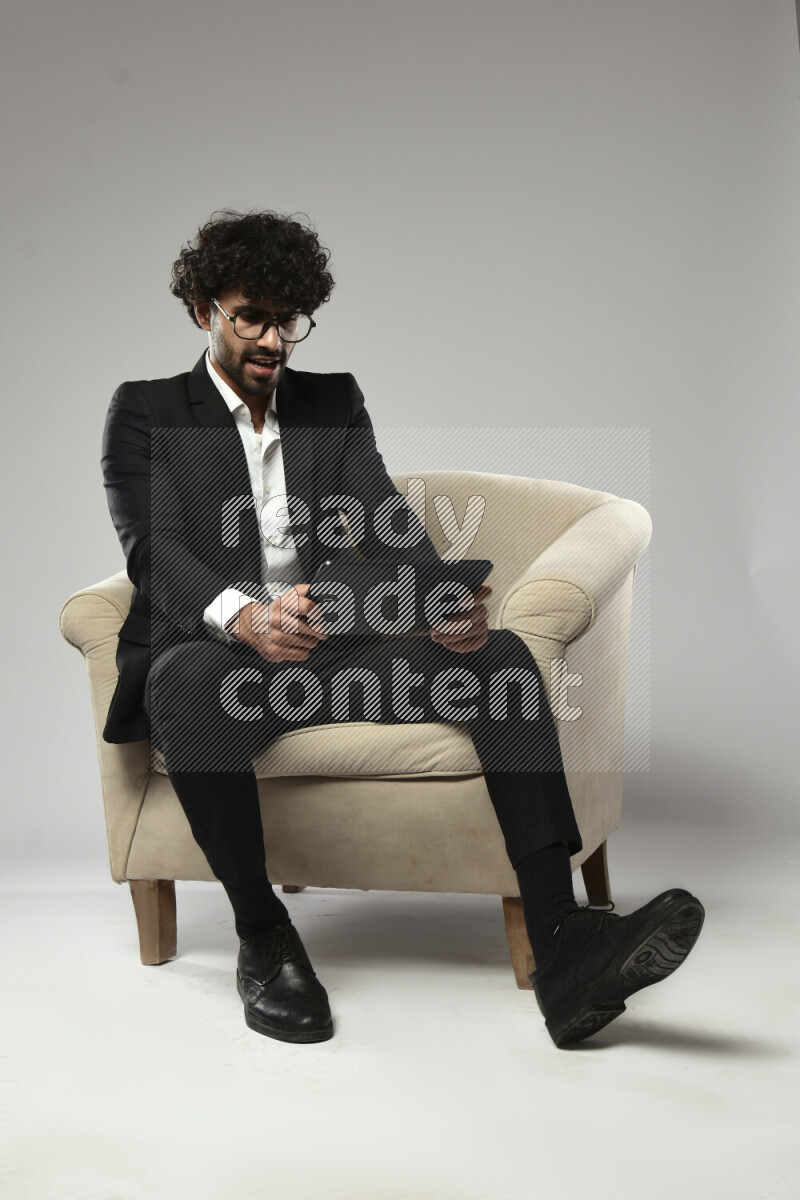 رجل يرتدي ملابس رسمية يجلس علي كرسي و يلعب علي تابلت علي خلفية بيضاء