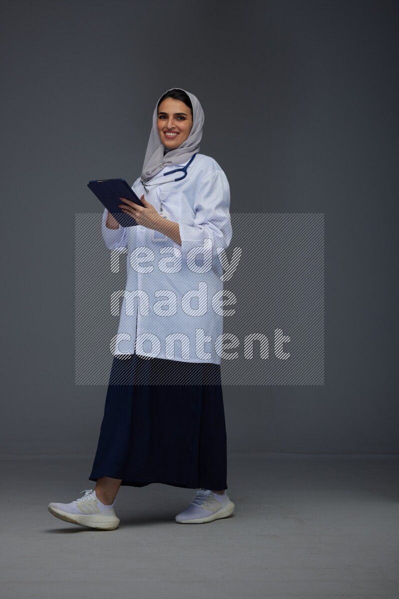 A Saudi doctor wearing a light gray head scarf standing and crossing her hands eye level on a grey background
