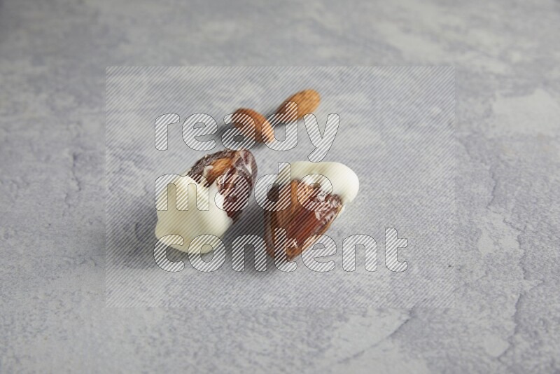 two almonds stuffed dates covered with white chololate with unroasted almonds on a light grey background