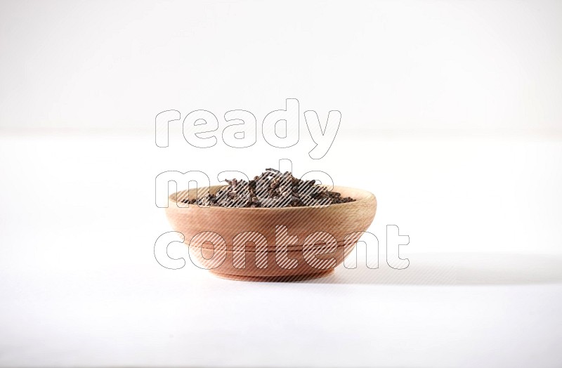 A wooden bowl full of cloves on a white flooring