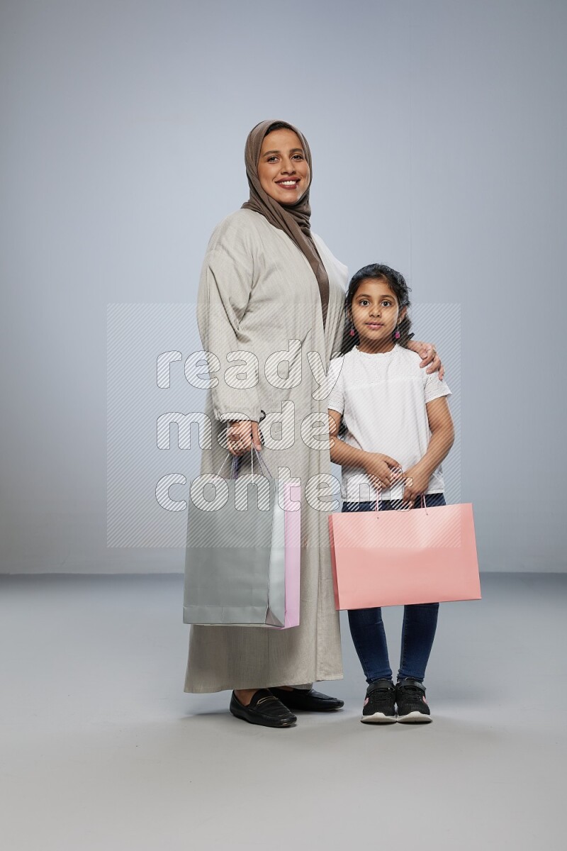 Mom and daughter holding shopping bags on gray background