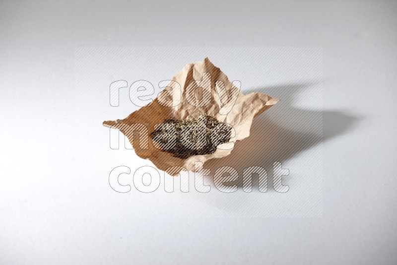 Cumin seeds in a crumpled piece of paper on white flooring