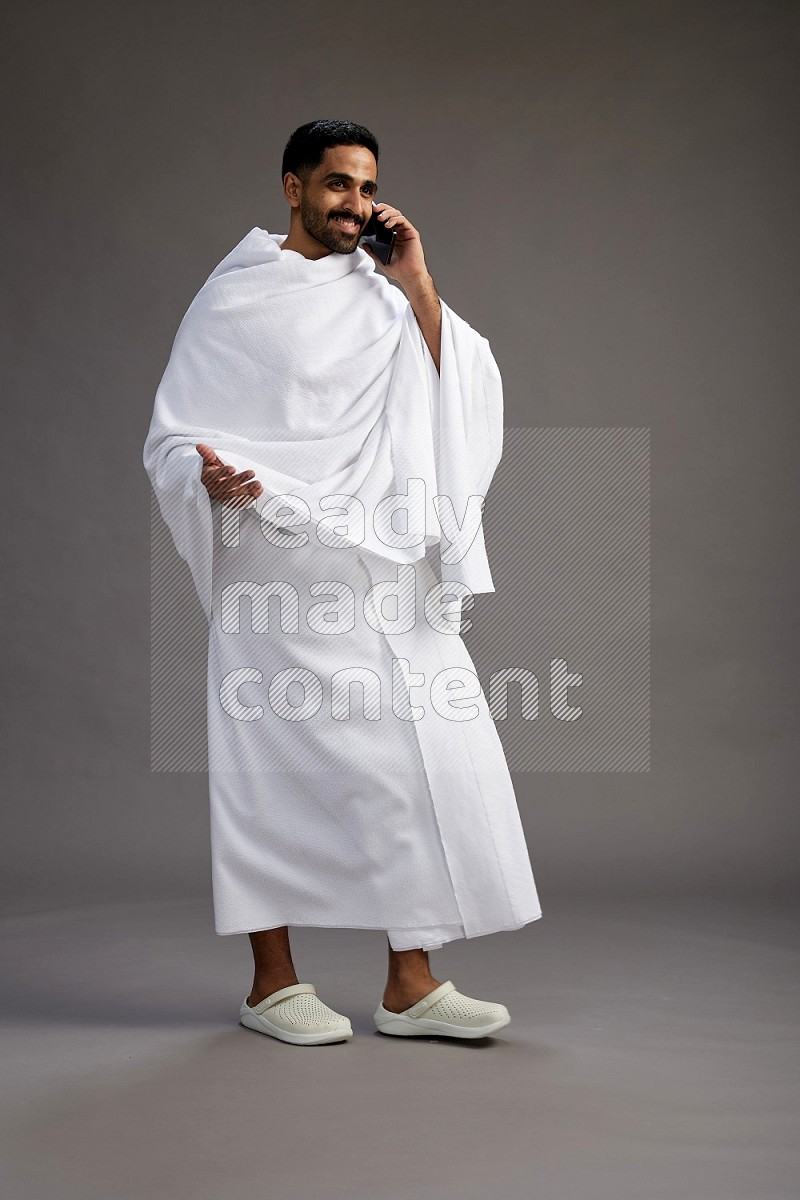 A man wearing Ehram Standing talking on phone on gray background