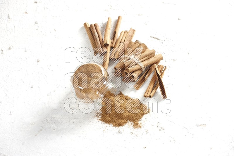 Flipped herbs glass jar full of cinnamon powder and cinnamon sticks in the back on a textured white background