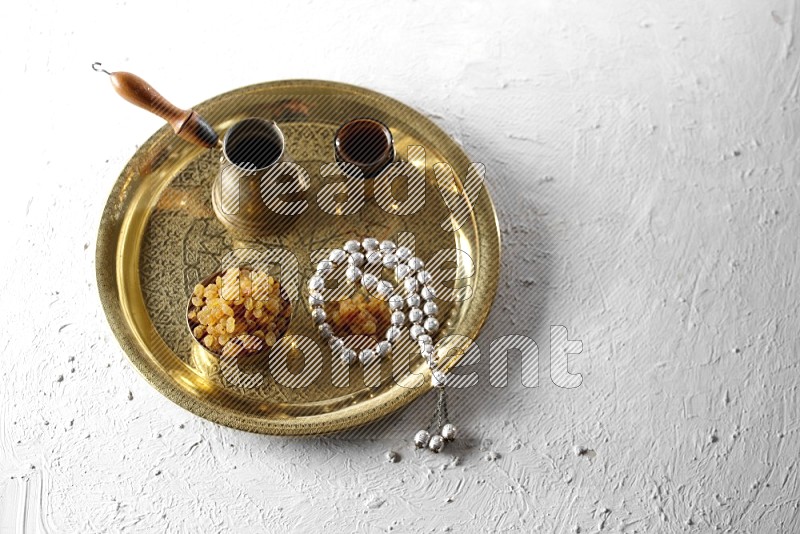 Raisins in a metal bowl with coffee and prayer beads on a tray in a light setup