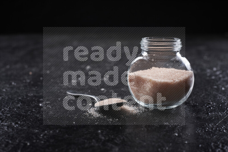 A glass jar full of fine himalayan salt on black background