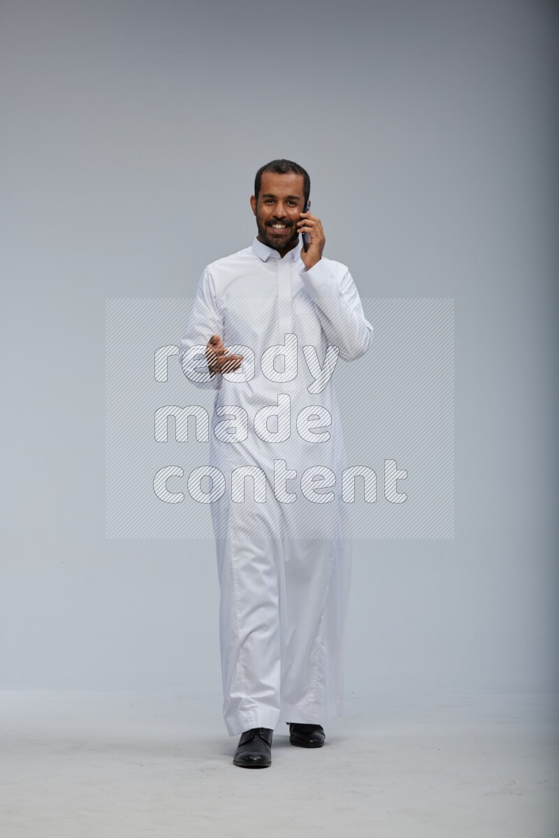 Saudi man wearing Thob standing talking on phone on Gray background