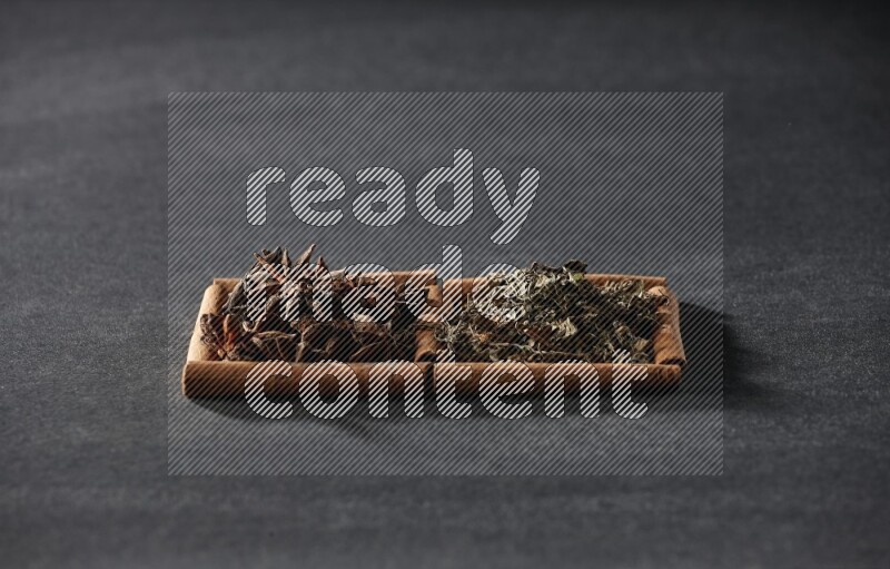 مربعان من أعواد القرفة ممتلئان باليانسون النجمي والريحان المجفف علي خلفية سوداء