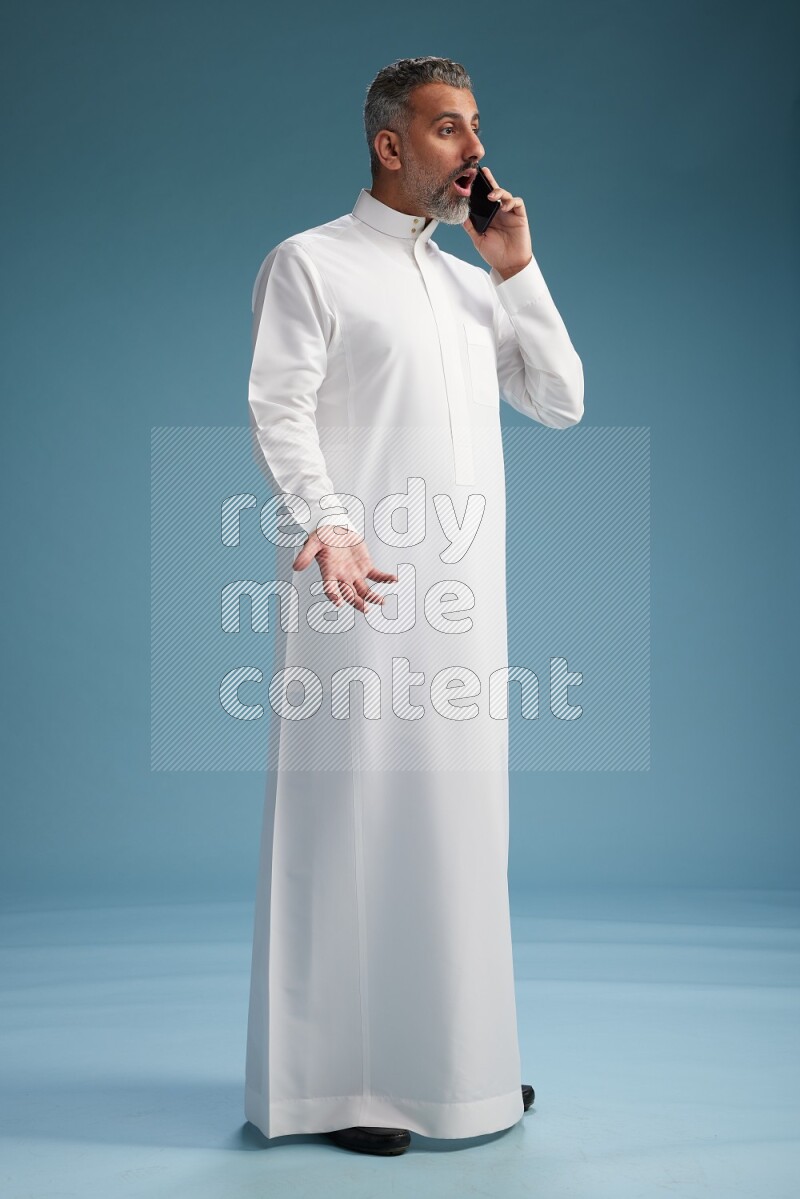 Saudi man wearing thob talking on the phone on blue background