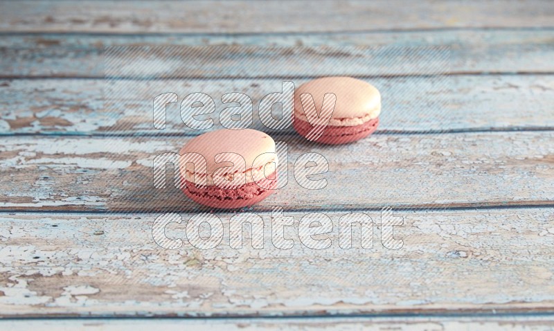 45º Shot of two Pink Litchi Raspberry macarons on light blue wooden background