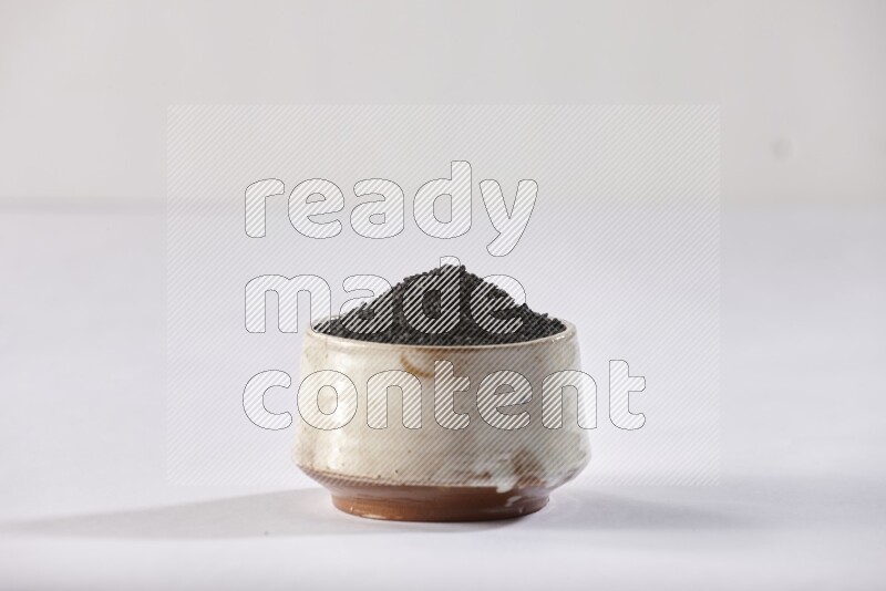 A beige pottery bowl full of black seeds on white flooring