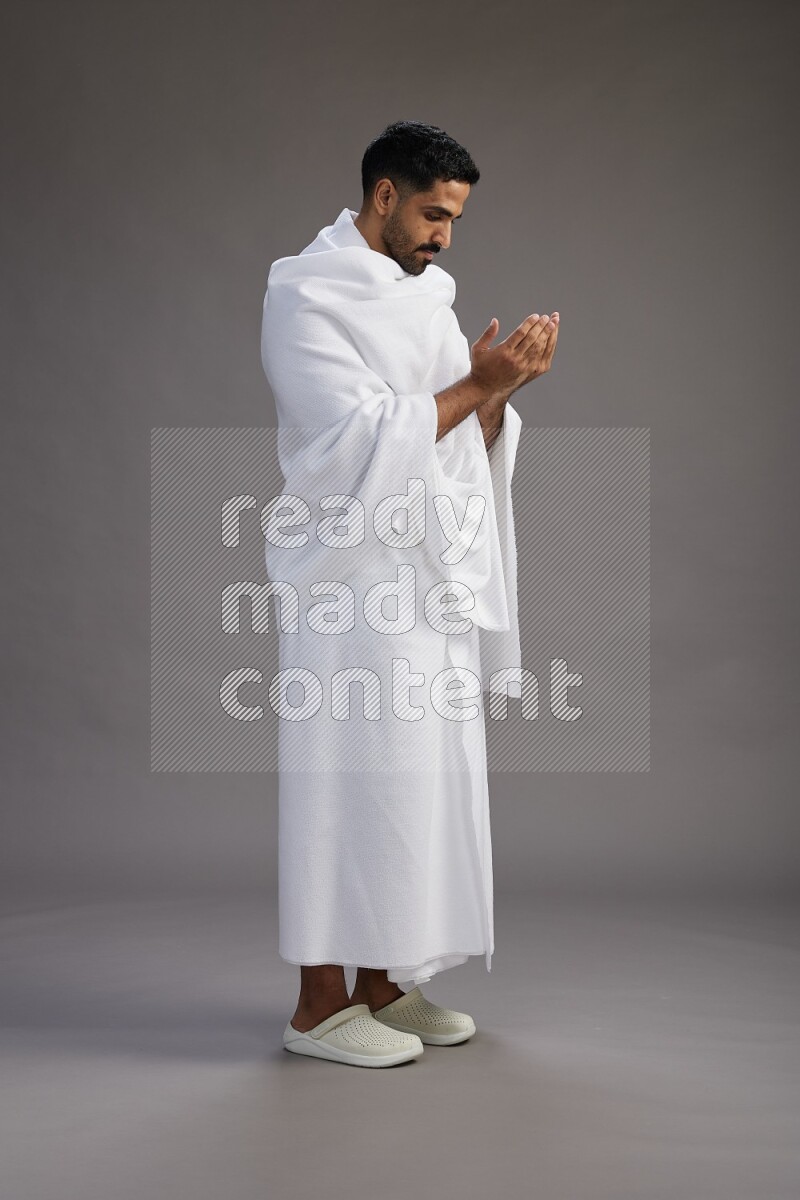 A man wearing Ehram Standing performing dua'a on gray background