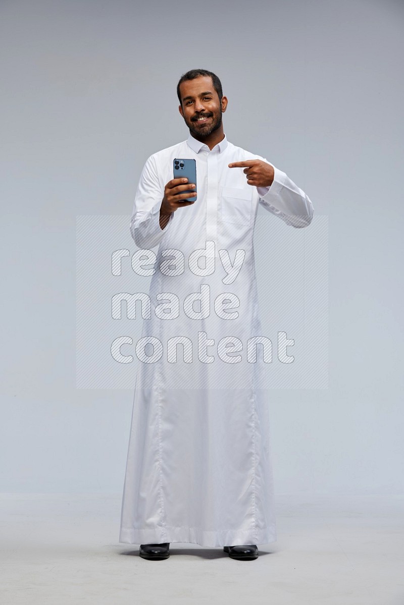 Saudi man wearing Thob standing texting on phone on Gray background