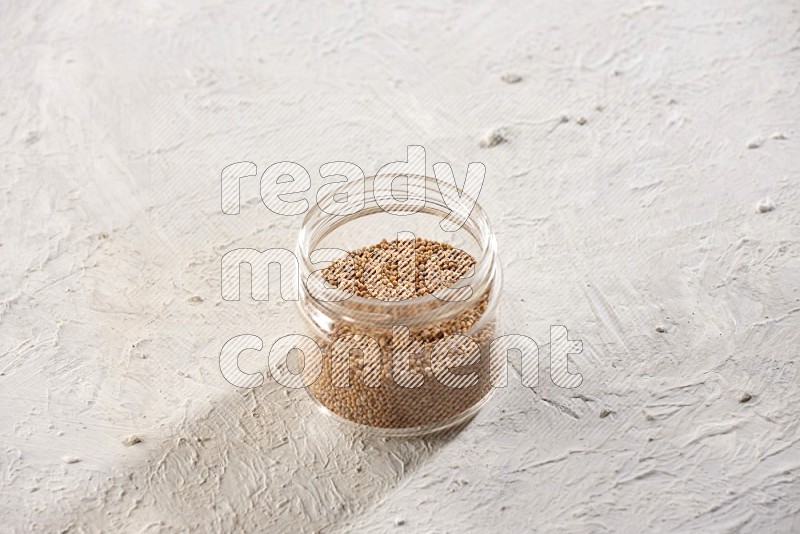 A glass jar full of mustard seeds on a textured white flooring in different angles
