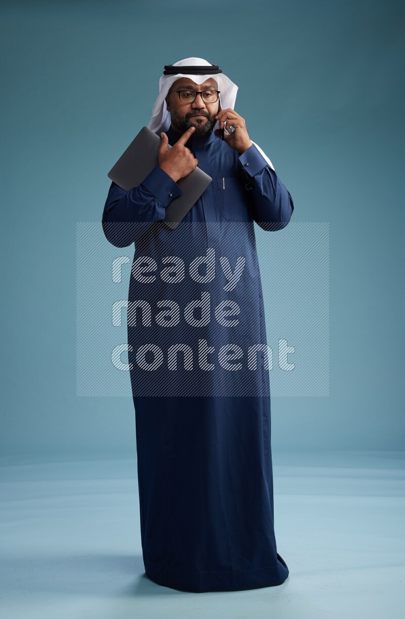 Saudi Man with shimag Standing talking on phone on blue background
