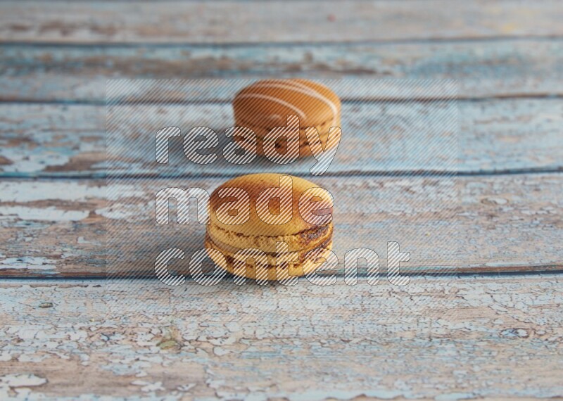 45º Shot of of two assorted Brown Irish Cream, and Yellow Crème Brulée macarons on light blue background